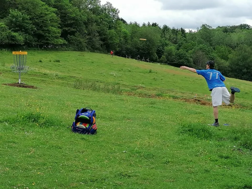 Un joueur lance un disque vers une corbeille de disc-golf dans une prairie
