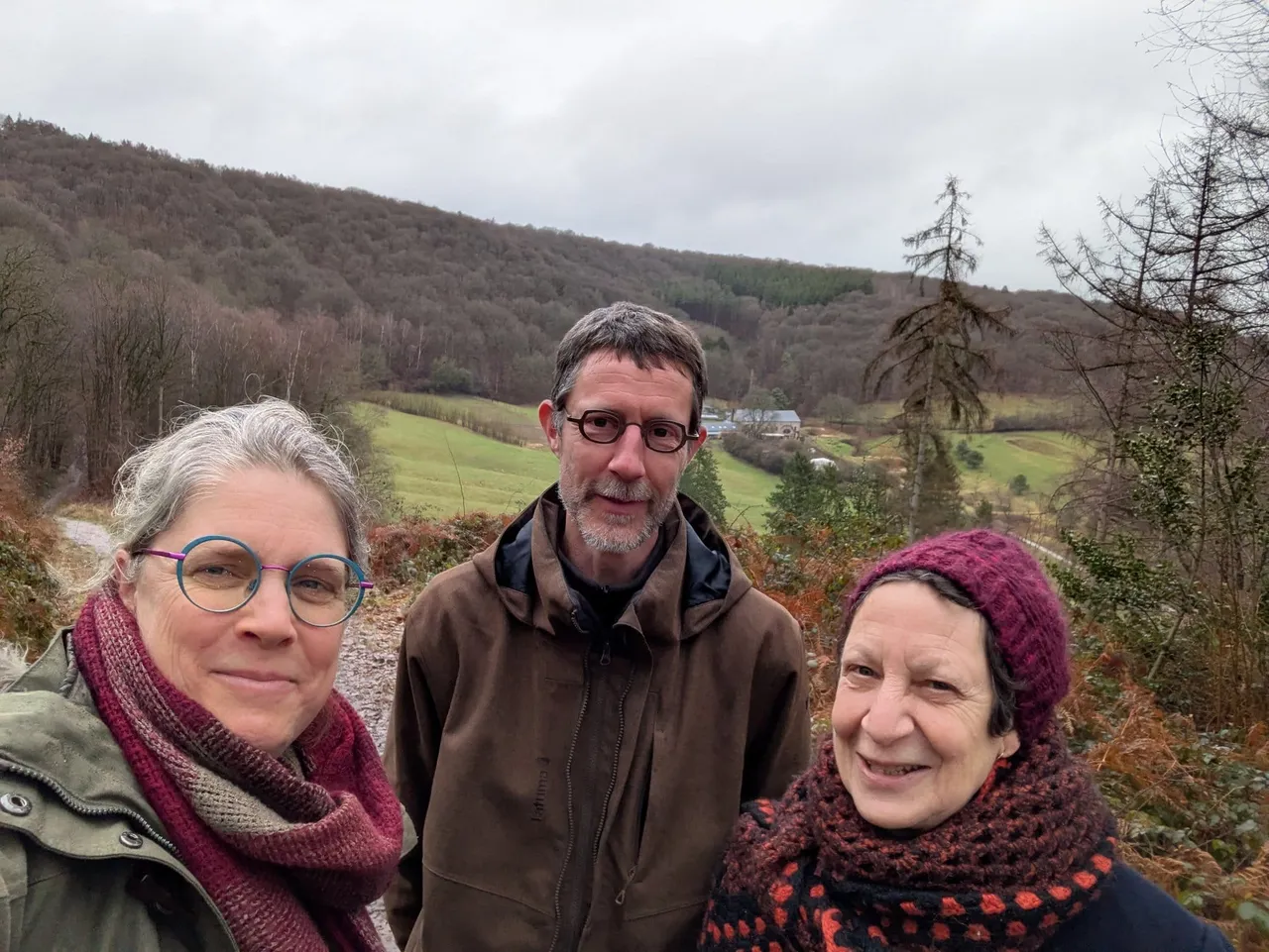 Trois personnes souriantes posent devant une vallée boisée